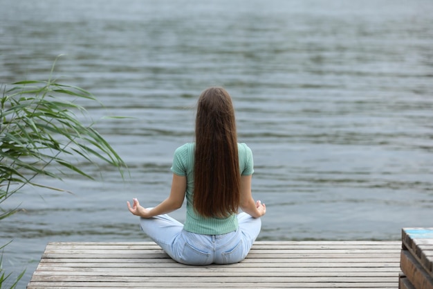 Adolescente meditando perto da vista traseira do rio