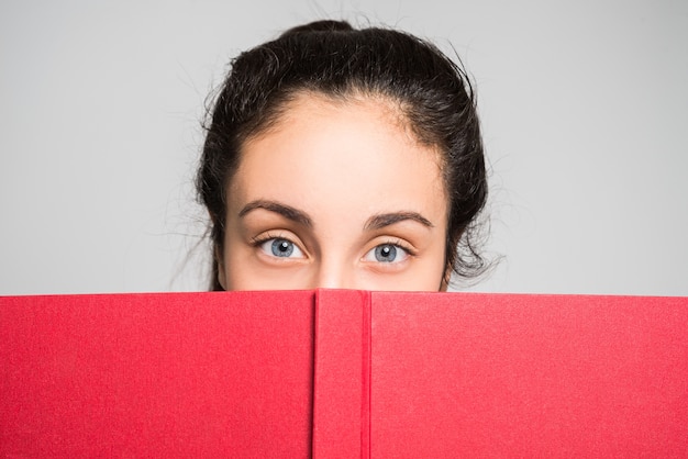 Foto adolescente mirando por detrás de un libro