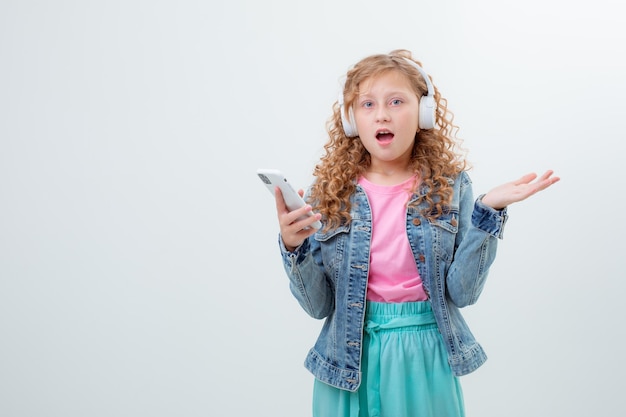 Una adolescente con una mochila en los auriculares sostiene un teléfono con un fondo blanco