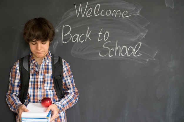 Adolescente con mochila, libros y manzana con regreso a la escuela en pizarra