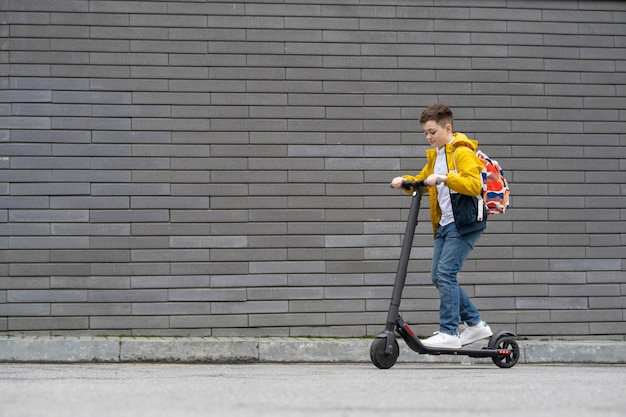 Adolescente con mochila paseos en scooter eléctrico sobre fondo de pared de ladrillo.