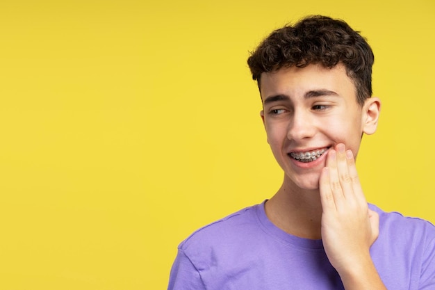 Adolescente molesto con aparatos ortopédicos tocando la mejilla con dolor de dientes mirando hacia otro lado