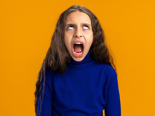 Adolescente molesto mirando hacia arriba gritando aislado en la pared naranja