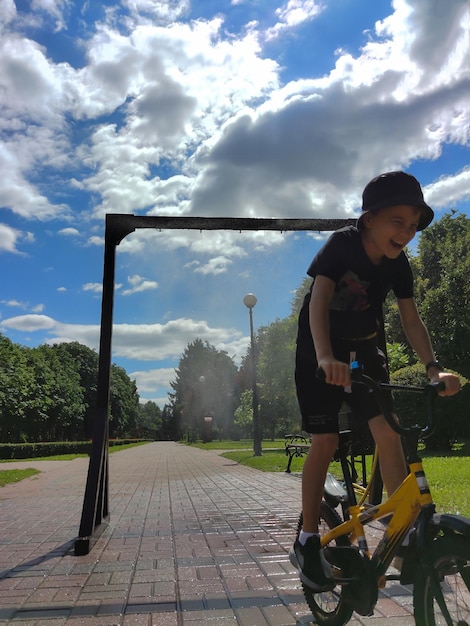 Un adolescente monta una bicicleta bajo un marco de enfriamiento en un parque de la ciudad y se ríe