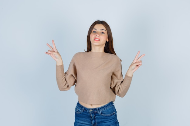 Adolescente mostrando gesto de vitória em suéter, jeans e orgulhoso, vista frontal.