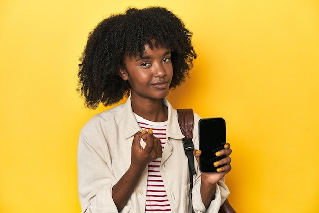 Adolescente mostrando mochila de smartphone em fundo amarelo apontando com o dedo para você