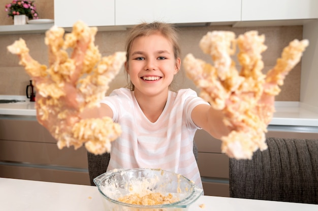 Adolescente muestra las manos sucias en masa divirtiéndose en la cocina