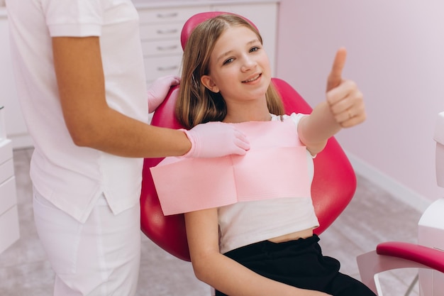 Adolescente muestra el pulgar hacia arriba y sonríe en la visita al dentista