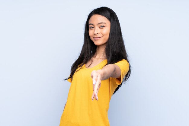 Adolescente mujer china aislada sobre fondo azul dándose la mano para cerrar un buen trato