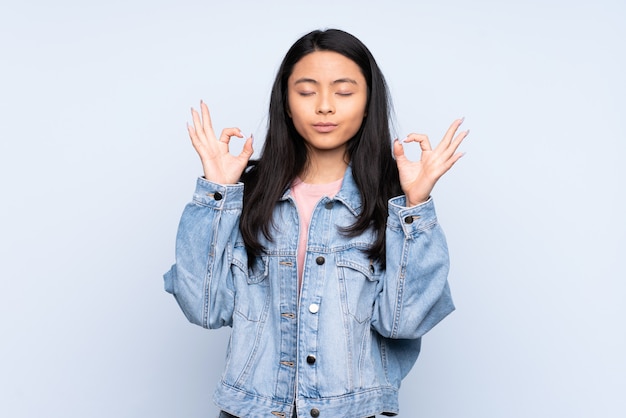 Adolescente mujer china aislada sobre fondo azul en pose zen