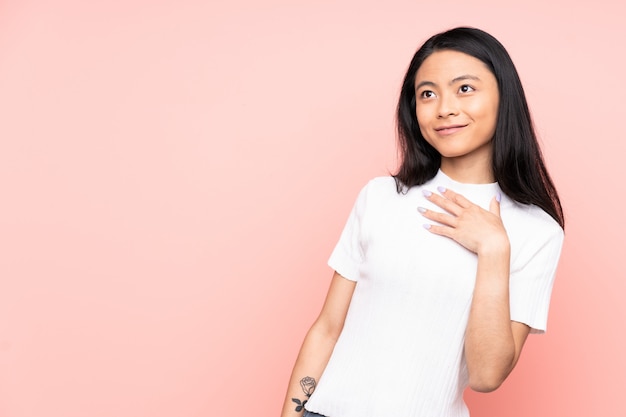 Adolescente mujer china aislada sobre fondo rosa mirando hacia arriba mientras sonríe