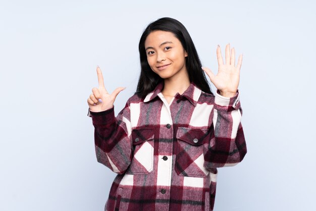 Adolescente mujer china en la pared azul contando siete con los dedos