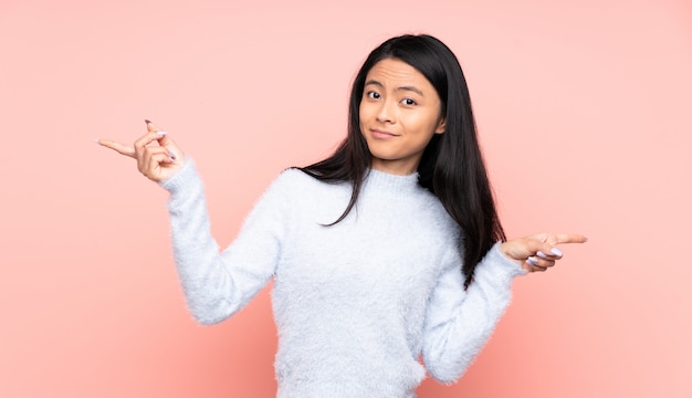 Adolescente mujer china en pared rosa apuntando el dedo a los laterales y feliz