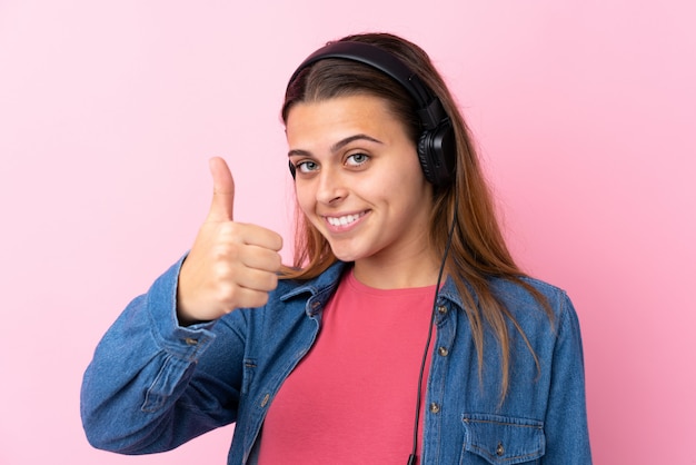 Adolescente mujer escuchando música sobre pared rosa aislado