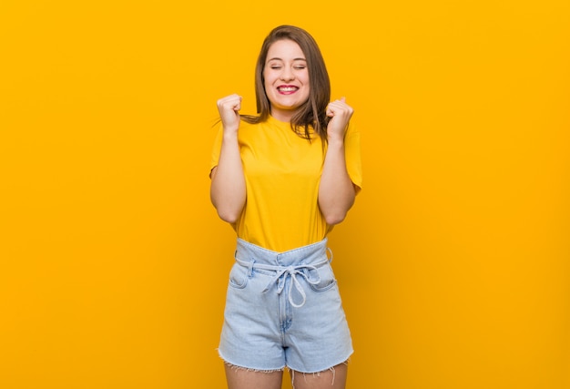 Adolescente mujer joven con una camisa amarilla levantando el puño, sentirse feliz y exitoso. Concepto de victoria