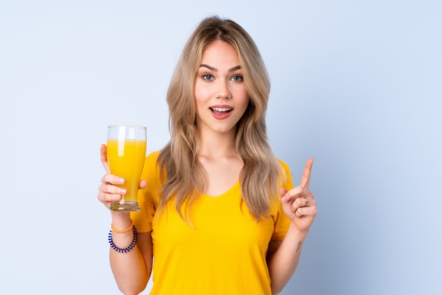 Adolescente mujer rusa sosteniendo un jugo de naranja aislado en la pared azul, apuntando hacia una gran idea