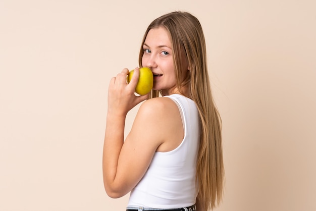 Adolescente mujer ucraniana aislada en espacio beige comiendo una manzana