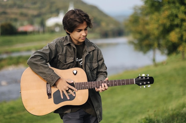 Adolescente músico concentrado tocando la guitarra acústica al aire libre chico guapo amor misuc