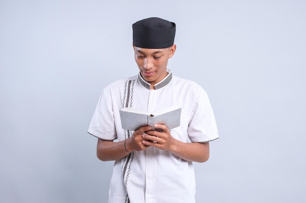 Un adolescente musulmán asiático lleva una gorra leyendo el Corán.