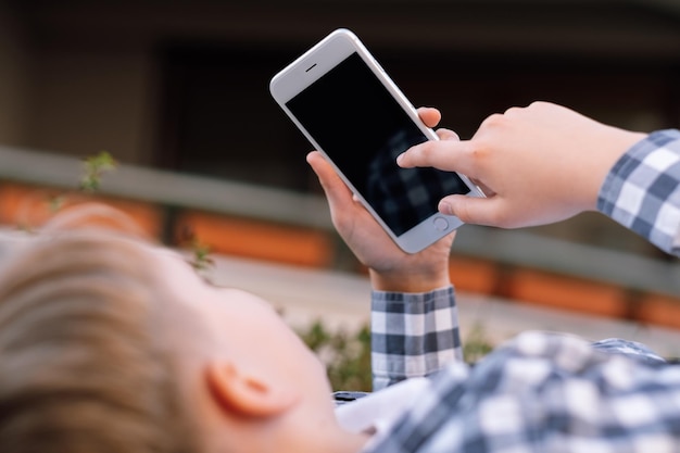 Un adolescente navega por Internet usando un teléfono inteligente mientras está acostado en un banco