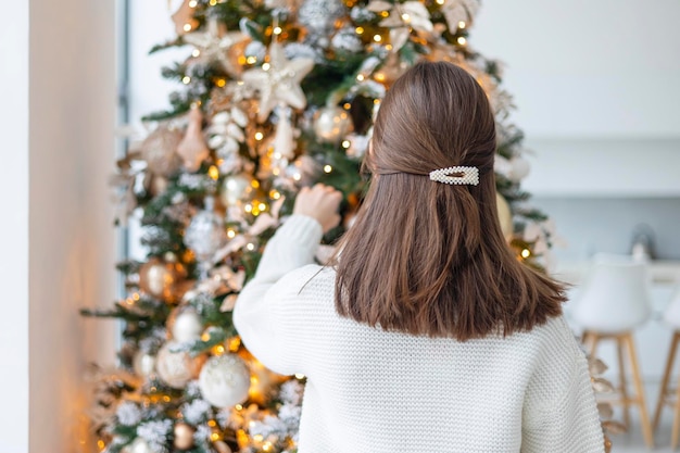Adolescente de Navidad en suéter de punto blanco está de pie en la sala de estar desde atrás