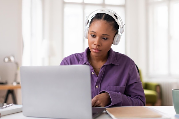 Adolescente negra concentrada estudiando con auriculares y portátil