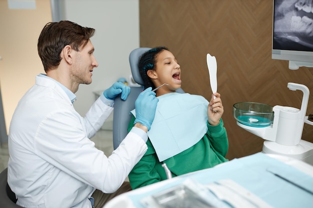 Foto adolescente negra mirándose en el espejo durante el chequeo dental en la clínica