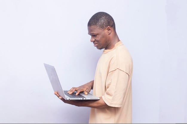 Adolescente negro angustiado sosteniendo y escribiendo en la computadora portátil con una expresión facial molesta