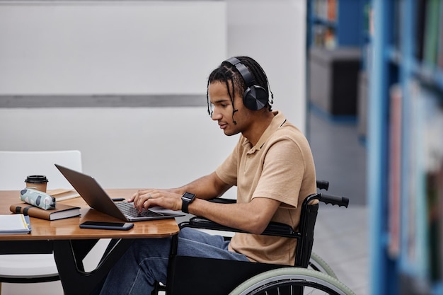 Adolescente negro com deficiência estudando na biblioteca da faculdade e usando laptop