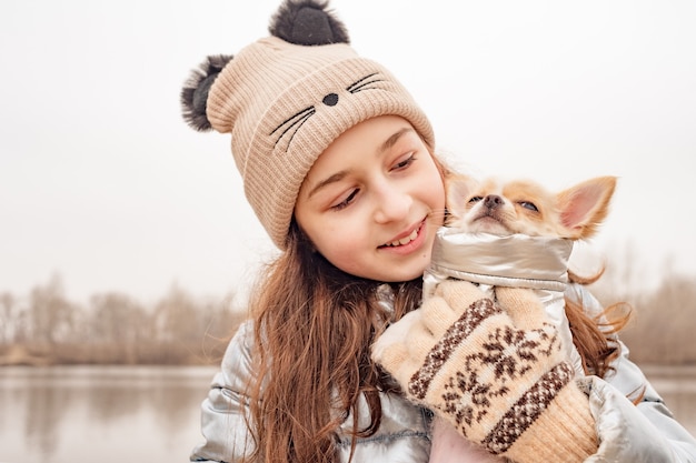 Adolescente niña y chihuahua. Chica con una chaqueta de invierno sobre un río con un perro.