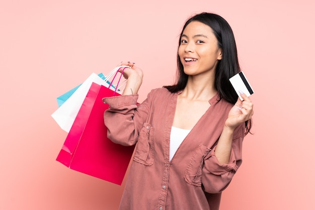 Adolescente niña china aislada en la pared rosa con bolsas de la compra y una tarjeta de crédito