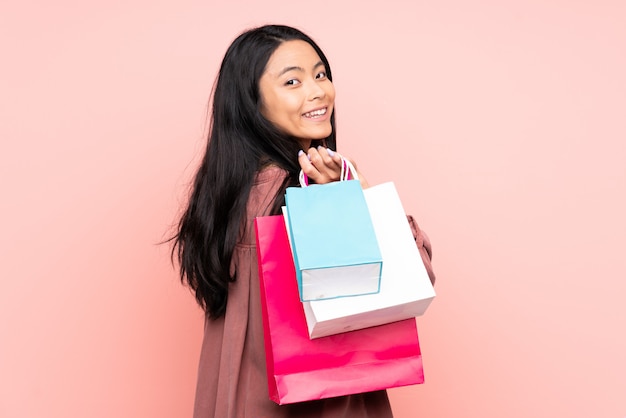 Adolescente niña china aislada en la pared rosa sosteniendo bolsas de compras y sonriendo