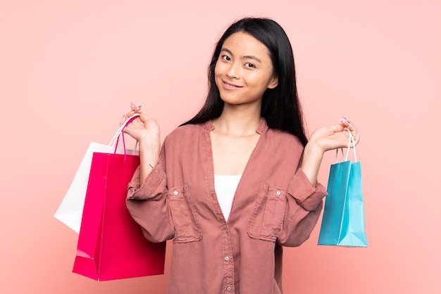 Adolescente niña china aislada en rosa sosteniendo bolsas de compras y sonriendo