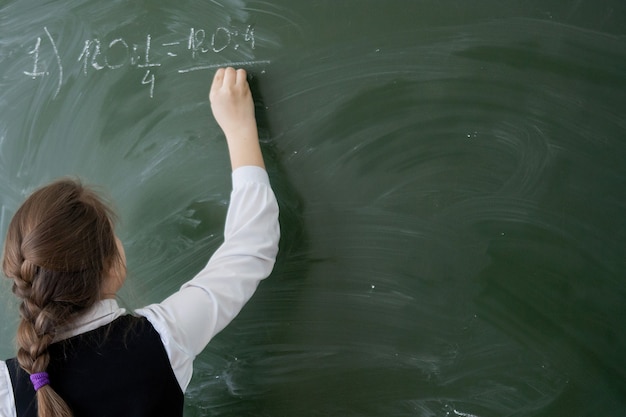 Adolescente niña Colegiala escribe en la pizarra en el aula en la lección. Educación, formación, cuidado de niños. Vista trasera. Foco seleccionado.