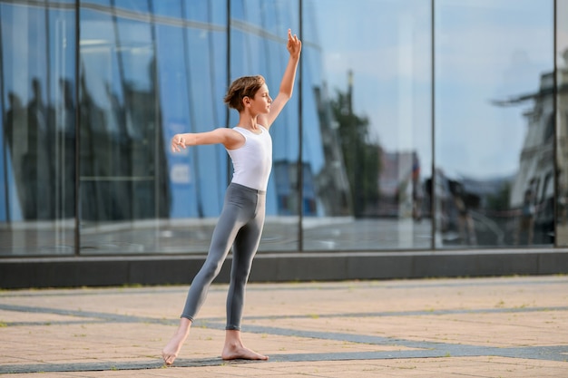 Adolescente niño de ballet bailando en el contexto del reflejo de la ciudad y el cielo en la pared de cristal