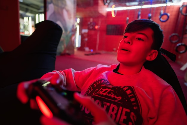 Adolescente niño jugador jugar consola de videojuegos gamepad en sala de juegos roja