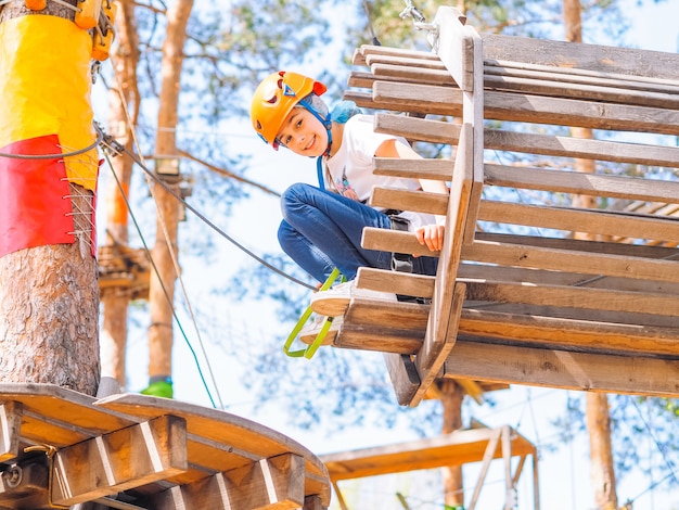 Adolescente no capacete laranja subindo nas árvores no parque de aventura na floresta.