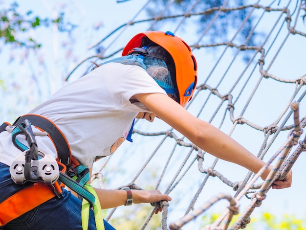 Adolescente no capacete laranja subindo nas árvores no parque de aventura na floresta.