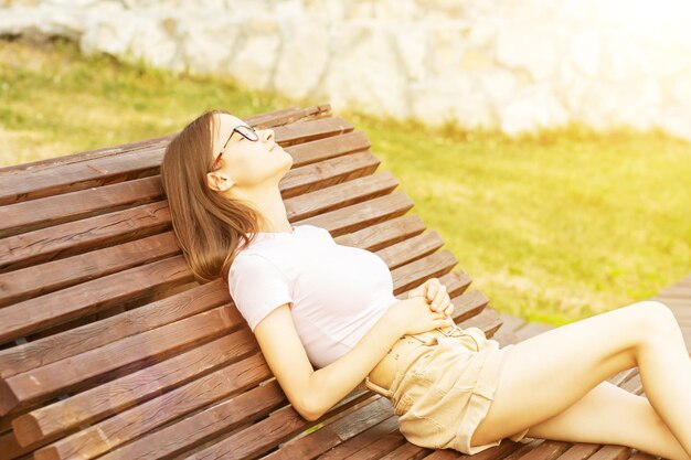 Adolescente no parque sorrindo em um banco relaxa em um dia ensolarado de verão