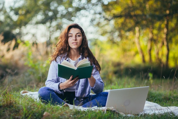 Adolescente nostálgico está sentado en el parque y leyendo un libro