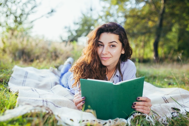 Foto adolescente nostálgico está sentado en el parque y leyendo un libro