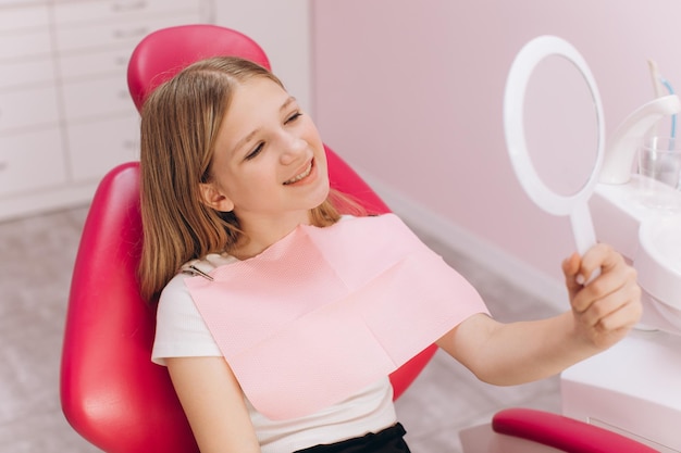 Adolescente olha no espelho durante uma visita a uma mulher dentista em uma clínica odontológica