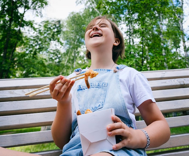 Una adolescente en un paseo en un día de verano en el parque almuerza con fideos wok