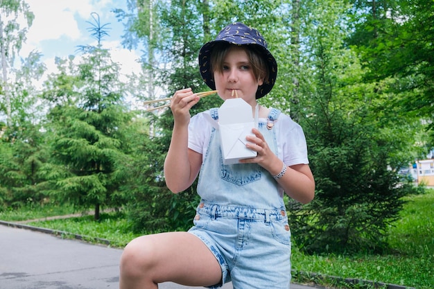 Una adolescente en un paseo en un día de verano en el parque almuerza con fideos wok