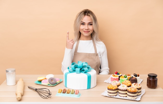 Adolescente pastelero con un gran pastel en una mesa señalando con el dedo índice una gran idea