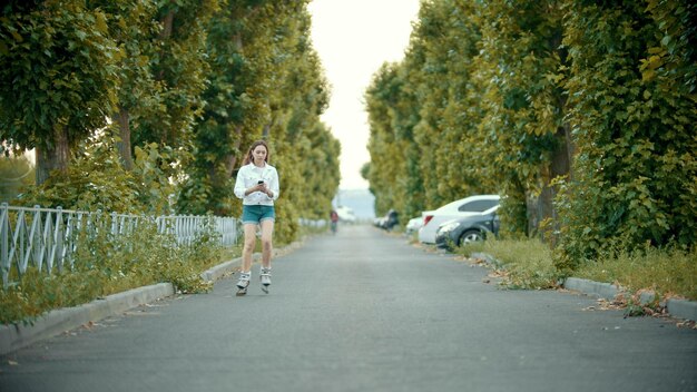 Una adolescente en patines patinando en la carretera mirando el teléfono