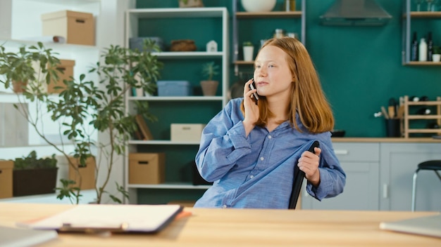 Foto adolescente pelirroja estudiando en casa en línea hablando por teléfono