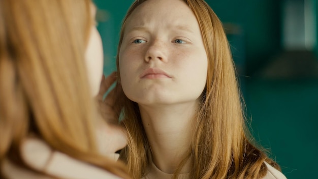 Una adolescente pelirroja examina su reflejo en el espejo adolescencia