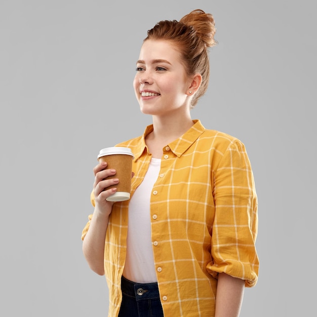 una adolescente pelirroja feliz con una taza de café de papel