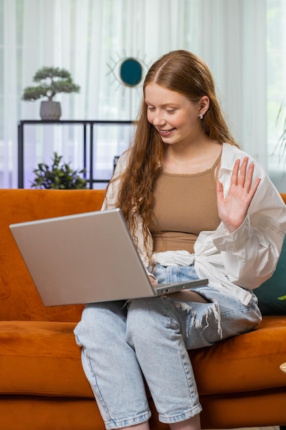 Adolescente pelirroja sentada en el sofá de casa haciendo una videoconferencia con amigos o familiares